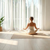 Person meditating beside a yoga mat in soft morning light for a calm, grounded practice.