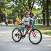 A kid rides a single-speed bicycle while a parent checks safety gear nearby in a park