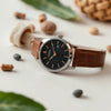 Quartz movement men’s wristwatch with a clean dial, slim metal case, and leather band on a light background