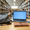 Slim laptop on a study desk in a campus library with a backpack and notebook nearby