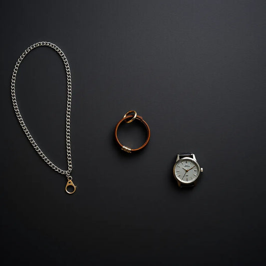 Silver chain, ring, leather bracelet, and wristwatch arranged neatly on a dark background for classic men’s jewelry styling.